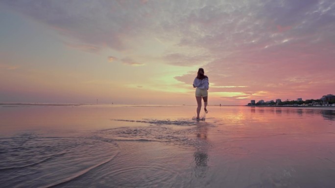 日落时分，年轻的赤脚长发女子在沙滩上奔跑