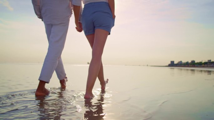 一对夫妇赤脚走在沙滩上，手牵着手