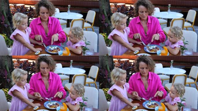年轻的母亲切下一块美味的煎蛋卷，在咖啡馆喂女儿。在夏日咖啡馆喂孩子的动态视频。母亲和女儿在咖啡馆度假