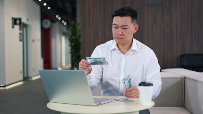 集中的亚洲人数了几百美元，发现了一张假钞。男雇主对拿着笔记本电脑和咖啡杯坐在办公桌前作弊感到不安。
