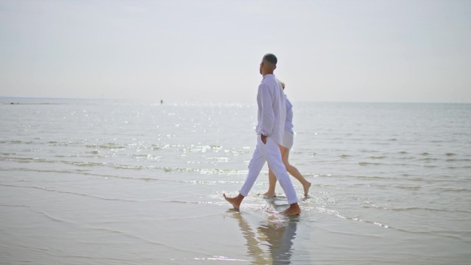 一对夫妇在阳光下赤脚走在沙滩上