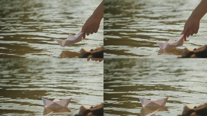 女子手把纸船放在公园的水上近距离观看。池塘上的折纸鹤。晴天的自然湖景