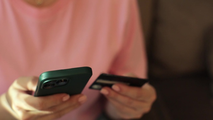 妇女手持智能手机和信用卡在家里网上购物的特写。智能手机购物网银服务理念。