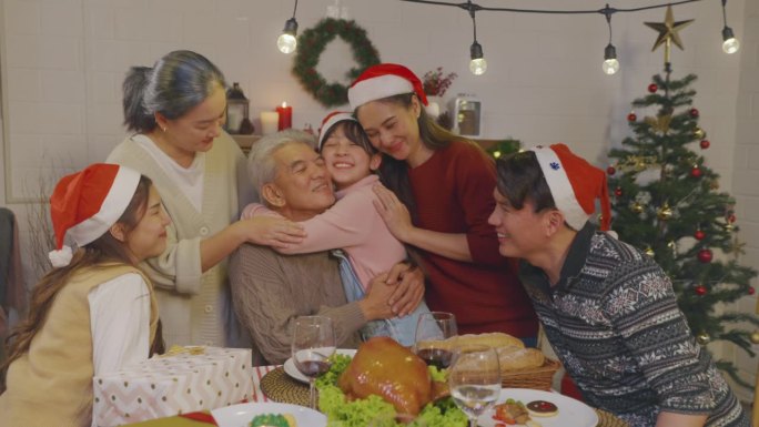 亚洲小孩在家里庆祝圣诞派对时拥抱爷爷奶奶。迷人的家庭在假期度过闲暇闲暇时间，在家里的餐桌上庆祝感恩节