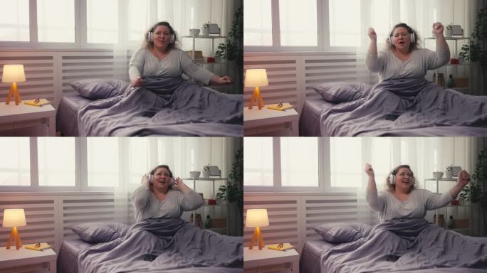 快乐的超重女人在手机应用上听着最喜欢的歌曲，在床上跳舞