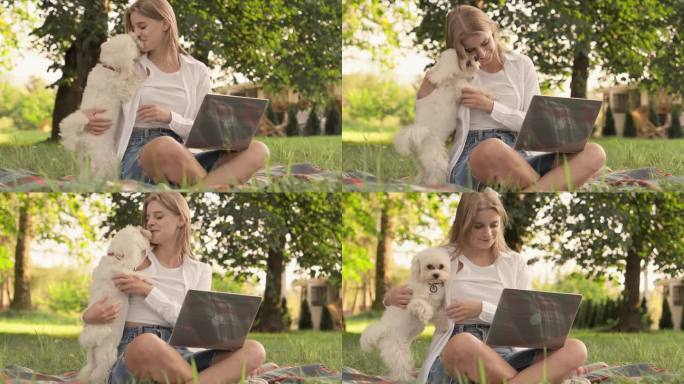 轻松的学习和放松:一位年轻的女学生在网上购物时享受公园、笔记本电脑和一只忠实的狗。他和他的小狗玩耍，