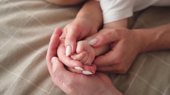 幸福的家庭。刚出生的小婴儿小手放在妈妈爸爸的手心上。父母握着新生儿的手。妈妈，爸爸，宝宝在家。支持保