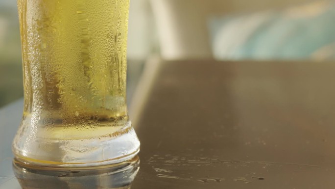 木桌上冰镇的、金黄的酿啤酒的玻璃底，冰凉的液体闪烁着一种闪闪发光的魅力，杯子里折射出一种庆祝和放松的