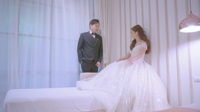 新娘坐在酒店房间的沙发上，新郎正在亲吻她的手。
