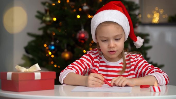 快乐的小女孩在圣诞树的背景下给圣诞老人写信