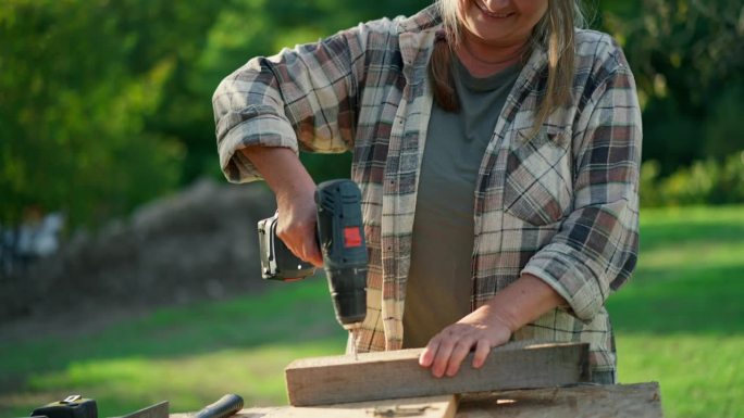 快乐手巧的女木匠在户外的木工diy车间用钻。