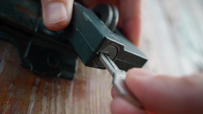 一只手将钥匙插入古董木门上的挂锁，特写。打开挂锁，透视视图