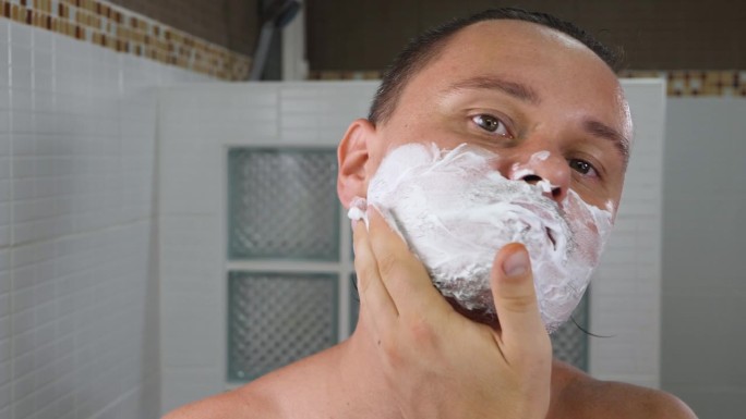 英俊的成年男子在脸上涂抹剃须泡沫