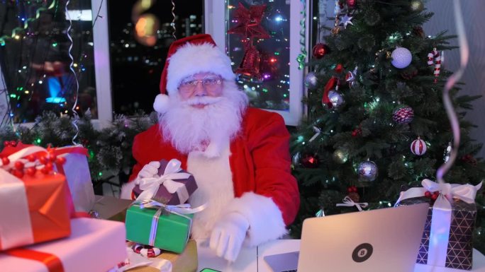 魅力十足的圣诞老人手里拿着礼物，坐在笔记本电脑前抚摸着胡须，气氛庄严而喜庆