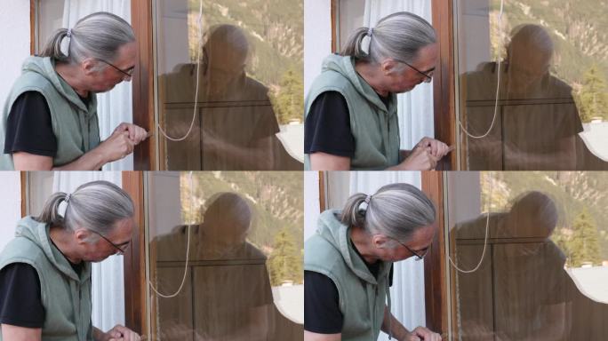 一位头发花白的男子正在清理自家阳台门上的旧硅胶绝缘材料，以备后续更换。