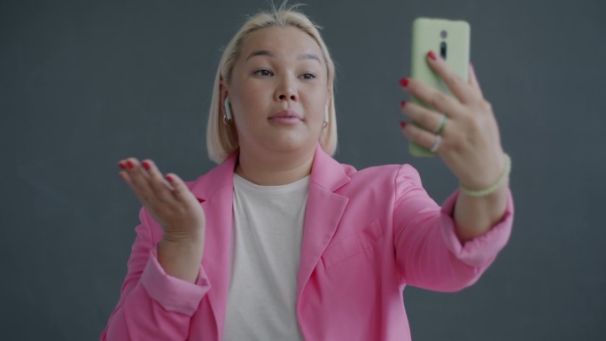 欢快的亚洲妇女用智能手机和无线耳机进行在线视频通话的慢动作肖像，有说有笑