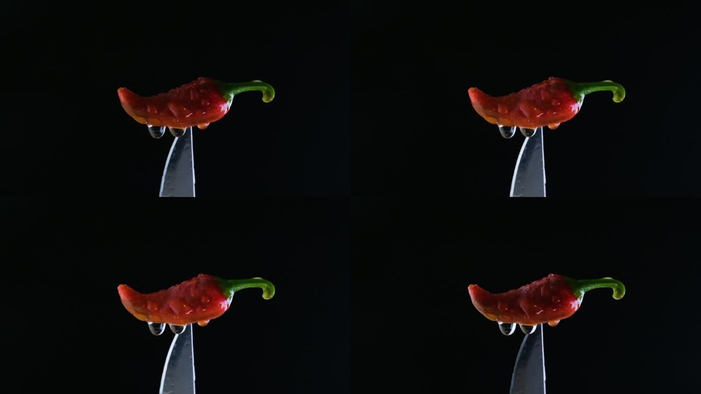 黑色背景上的红色湿墨西哥胡椒被一把银色的刀从底部捏起，镜头从左下角发出闪光。