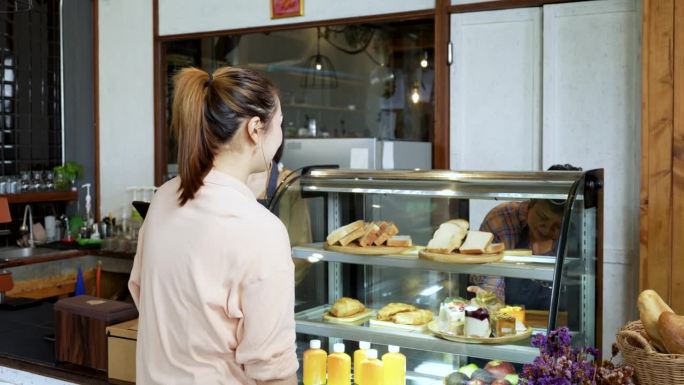 漂亮的亚洲女性顾客在面包店和咖啡店买蛋糕。上了年纪的店主围裙里的小贩在面包房卖糖。小生意。购物的概念