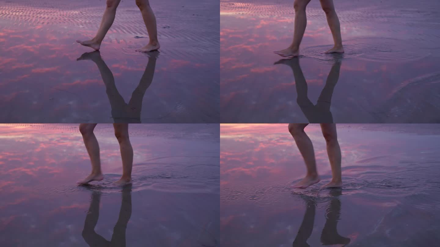 在紫色的夕阳下，女性的腿在浅水的沙滩上行走