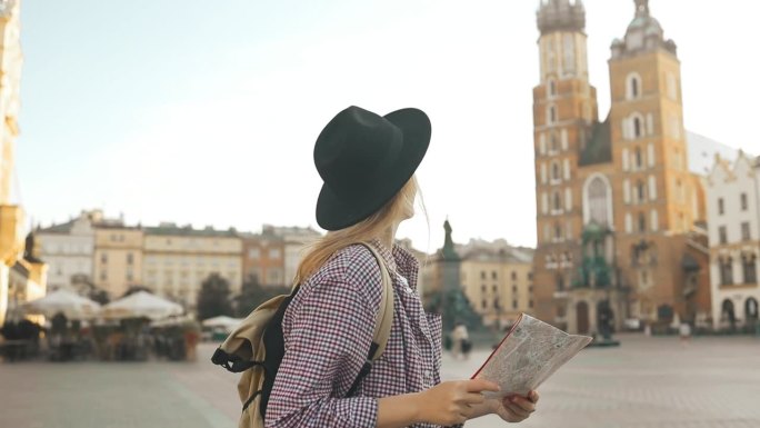 手持旅游地图走在克拉科夫旧市场广场上的女游客的真实照片。旅行和积极的生活方式理念。