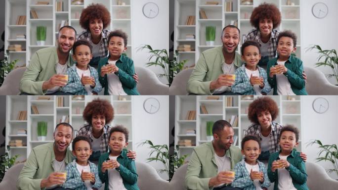 快乐的非裔美国夫妇和孩子的肖像，在家里喝着新鲜的果汁，对着镜头微笑。年轻漂亮的家庭妇女抱着孩子和兴奋
