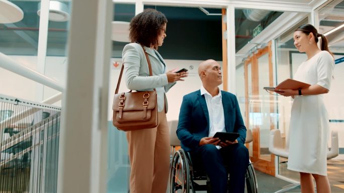 坐在轮椅上的残疾或残障商人在办公室里与同事讨论。员工们拿着手机和平板电脑，为即将到来的商业项目集思集