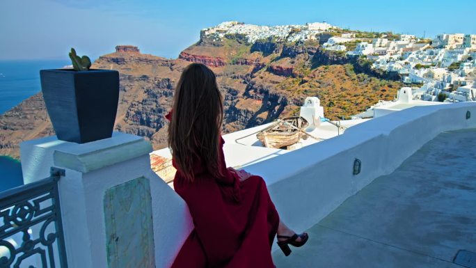 一个穿着红裙子的漂亮女孩正在欣赏圣托里尼岛的景色。