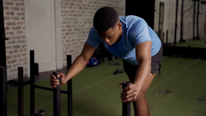 意志坚定、肌肉发达的年轻黑人在健身房做雪橇推运动
