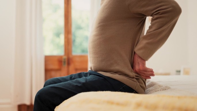 手，男人和疼痛在家里从背部，肌肉损伤或疲劳的风险脊柱侧凸在卧室。特写，不良姿势和拉伸脊柱纤维肌痛，骨