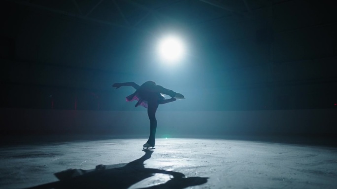 优雅的女性轮廓在溜冰场在黑暗中，慢动作，美丽的女人花样滑冰运动员旋转