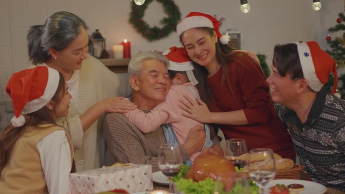 亚洲小孩在家里庆祝圣诞派对时拥抱爷爷奶奶。迷人的家庭在假期度过闲暇闲暇时间，在家里的餐桌上庆祝感恩节