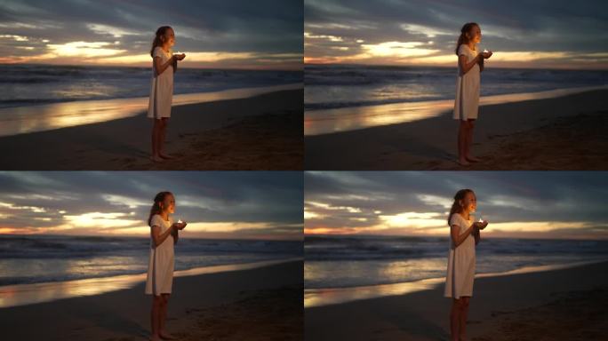 小女孩望着别处，手拿蜡烛站在沙滩上