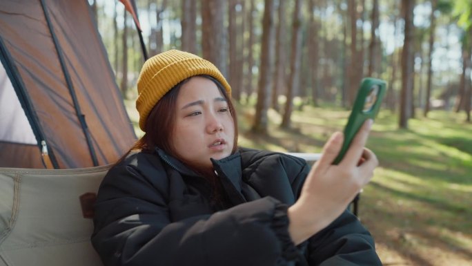 年轻的亚洲女游客在露营时使用手机，失去了信号。女性独自旅行和露营时混淆了电话、问题或信号差。网络问题