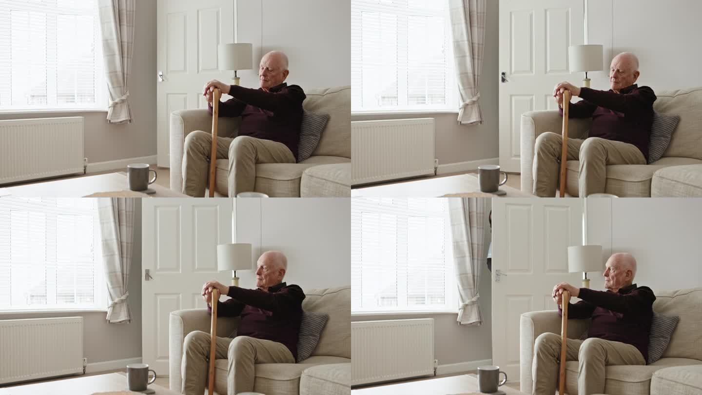 老人，拄着拐杖，在家里的沙发上思考，在照顾者的支持下或孤独地退休。老年人、痴呆症患者和有残疾的老年人