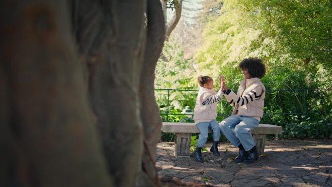 周末一家人坐在公园长椅上玩馅饼蛋糕。非洲母亲带着女儿