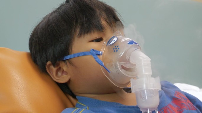 一名患有哮喘的亚洲男孩在医院接受喷雾器治疗。