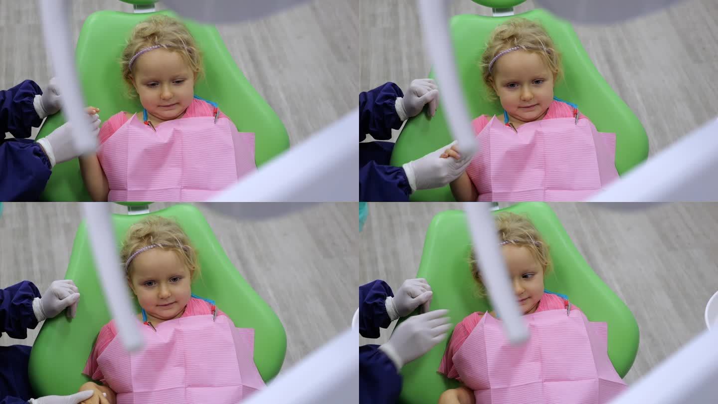 动态视频担心的小女孩坐在牙科椅上，手牵着牙医。善良的牙医医生在治疗前的激动时刻与孩子交谈，支持她的特