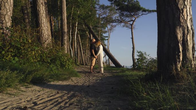 一对幸福的男女手牵着手站在海边的林间小路上。
