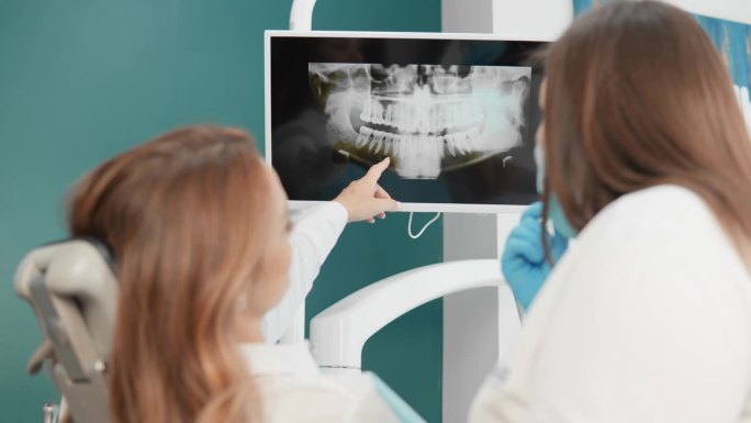 牙医给病人看口腔x光片以作诊断。牙医向病人解释牙齿和牙龈的断层扫描结果。病人在分析牙齿的x光片时信任