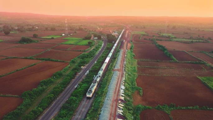 无人机拍摄的印度铁路客运列车在日落时分从印度瓜廖尔的一座公路桥下通过