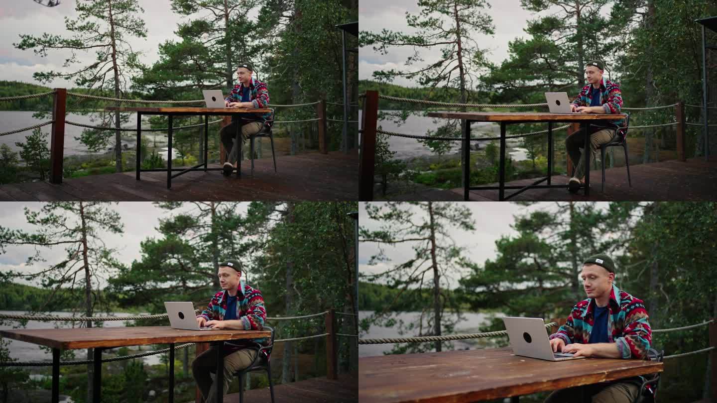 年轻的成年男子坐在大房子的露台上，用笔记本电脑工作，在网上休息