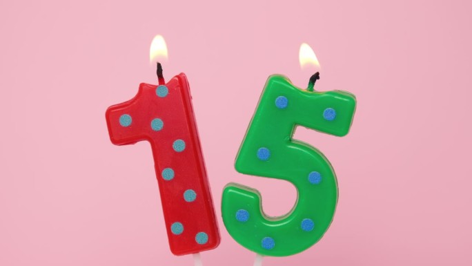 十五周年纪念视频横幅燃烧斑点红色和绿色数字十五蜡烛在浅粉红色的背景。4K分辨率生日快乐横幅