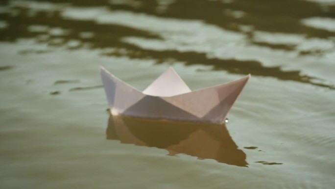 一个女人在公园里把纸船放在水面上。池塘上的折纸鹤。晴天的自然湖景