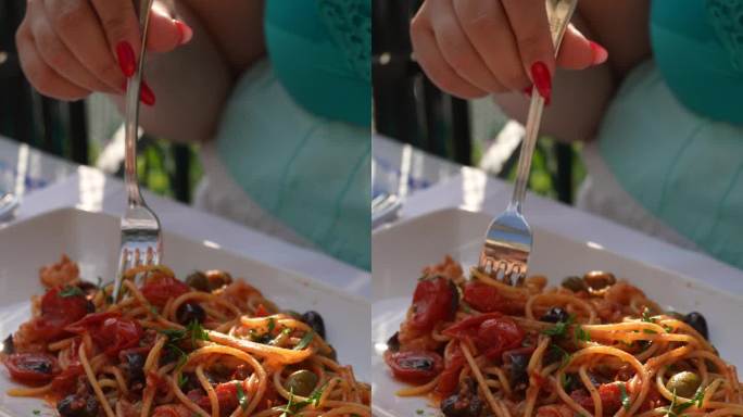 特写垂直剪裁的照片，一个不知名的女人坐在户外咖啡馆的桌子上，用叉子包着意大利面和海鲜