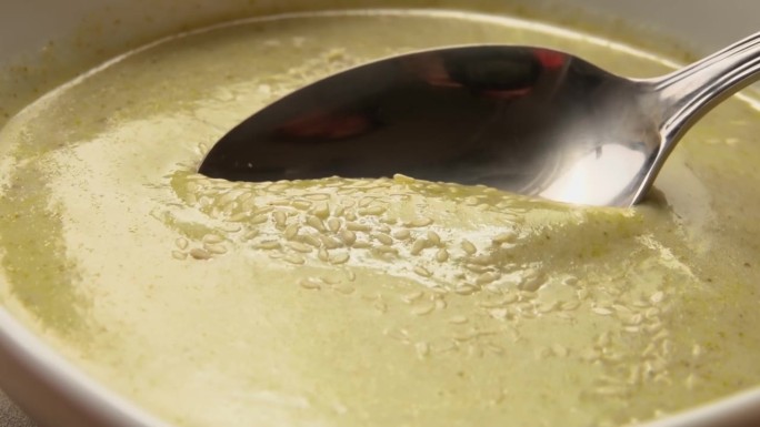 用勺子舀起表面有芝麻的西兰花汤