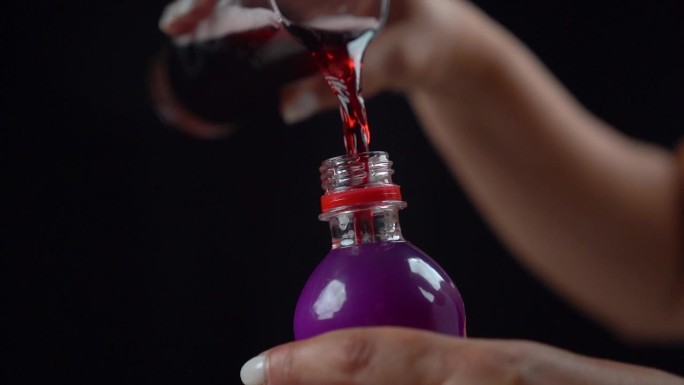 把红色的碳酸饮料从玻璃杯倒回紫色的塑料瓶里