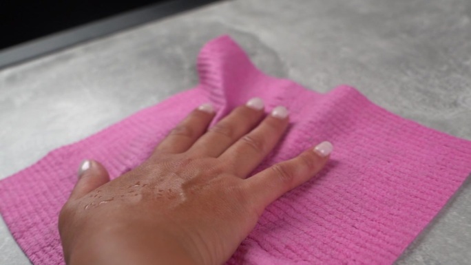 女人用涂了指甲油的手用粉红色的清洁布擦拭灰色的桌子