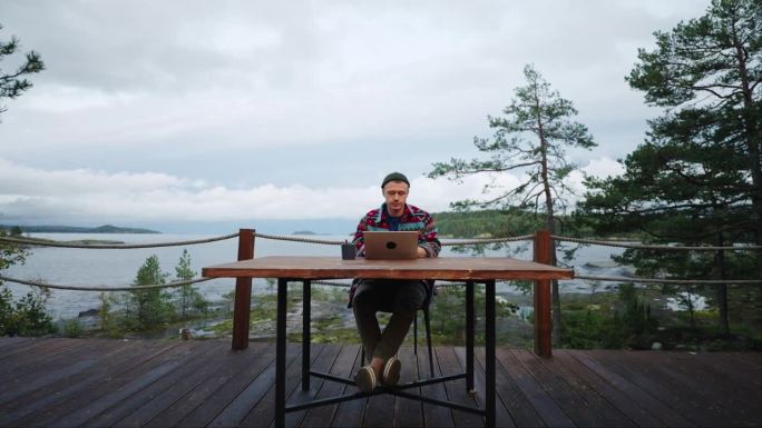 帅哥上网冲浪或在阳台上用笔记本电脑工作与美丽的景色，斯坦尼康多莉拍摄