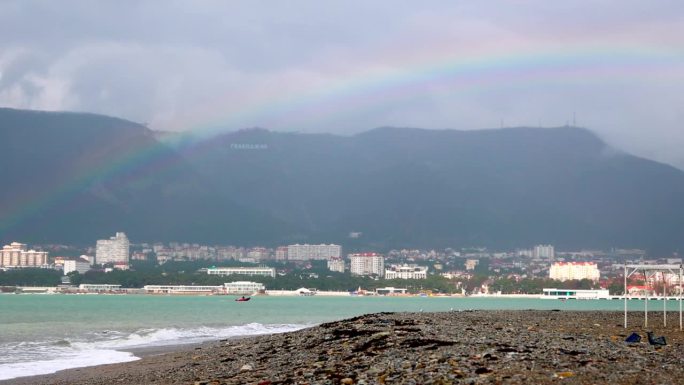 暴风雨过后冬天卵石沙滩上的彩虹。背景是乌云中的山脉。