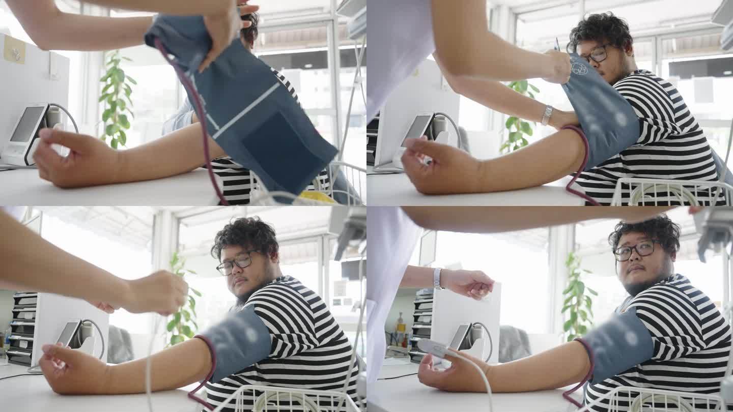 从低角度看，一个超重的亚洲男人坐在医生的办公室里，护士正在用血氧计测量血压